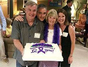 Friends and family pose with celebration cake for 12-year pancreatic cancer survivor