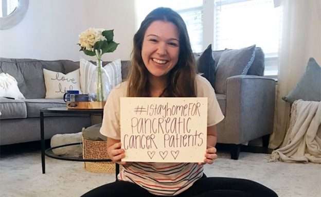 Young woman at home holding sign, “I stay home for pancreatic cancer patients” during pandemic