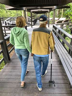 Wife and ailing husband shown from the back, walking together.