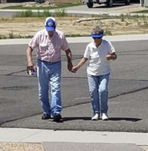 Caucasian couple in their 80s walking across wide, paved suburban street